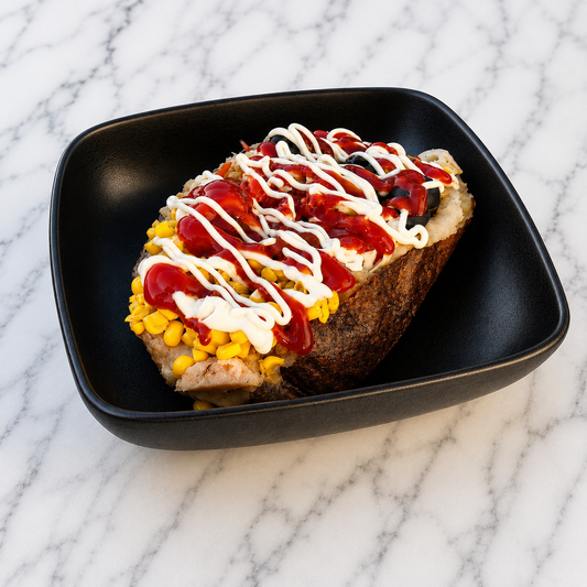 Classic Kumpir topped with condiments on a black plate on a marble surface